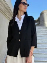 Blazer negro de lino con corte clásico, solapas de muesca, cierre con dos botones color madera, mangas 3/4 y bolsillos de parche frontales.