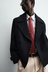 Abrigo corto azul marino de corte relajado, confeccionado en tejido con lana. Tiene cuello con solapas de pico, mangas largas con puños ajustables con trabilla, bolsillos de solapa en la cadera, bolsillo interior, abertura en el centro de la espalda y cierre frontal con botonadura.