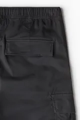 Pantalón cargo negro de corte slim fit, con cintura elástica ajustable con cordón, bolsillos laterales, bolsillos cargo con solapa y botones a presión ocultos, y pinzas en las rodillas.