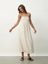 Vestido midi de color naranja, con escote recto y tirantes finos que se anudan sobre los hombros. Posee una cintura entallada con frunces que dan paso a una falda fluida.