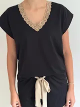 Conjunto de pijama de dos piezas color negro, compuesto por una remera de manga corta con escote en V adornado con puntilla beige, y un short con lazo frontal beige y terminación de puntilla beige en el ruedo.