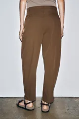 Pantalón marrón de tiro medio con trabillas en la cintura, bolsillos laterales, pinzas delanteras y bajo ajustable con trabilla y botón.