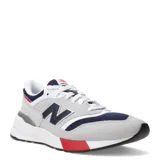 Championes New Balance modelo 997R, color gris con detalles en azul marino y rojo. Confeccionados en gamuza y malla, con logo "N" característico en los laterales.