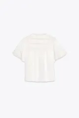 Top de tejido satinado color blanco, con cuello redondo, manga corta y detalle de puntilla a tono. Cierre frontal con lazadas.