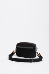 Bolso bandolera mini de nylon negro, con estructura blanda y cierre de cremallera. Posee una correa regulable de tejido negro con hebilla metálica plateada y un detalle de cuero sintético marrón en la correa. Lleva el logo metálico de Bimba y Lola en la parte frontal inferior.