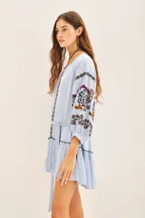 Vestido corto de bambula color celeste claro con bordados florales multicolor en el frente y mangas. Presenta escote redondo con cartera, cinturón de tela ajustable y volado en el ruedo.