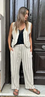 Conjunto de lino color crudo con rayas verticales negras, compuesto por un chaleco con botones y un pantalón de corte recto con cintura elastizada y cordón ajustable.