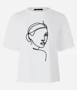 Remera blanca de algodón con cuello redondo y bordado de una cara de mujer con caravana dorada.