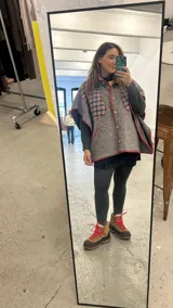Poncho de paño gris con apliques de tela escocesa y bordado artesanal en color rojo. Tiene cuello alto, cierre con botones de madera y mangas 3/4.