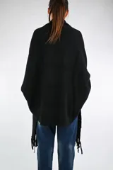 Ruana de punto color negro con flecos en el ruedo y mangas largas ajustadas con acabado acanalado. Presenta un diseño envolvente y abierto sin botones.