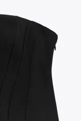Vestido corto negro sin mangas, con escote palabra de honor y pespuntes marcados. Cierre trasero con cremallera oculta.