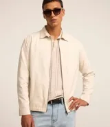 Campera color crema de sarga lisa, con cuello camisero, cierre frontal con cremallera, bolsillos delanteros, puños abotonados y bajo elástico.