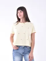 Remera de manga corta color amarillo pálido, con cuello redondo y pequeños bordados de cerezas rojas distribuidos por toda la prenda.
