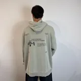 Canguro color gris claro con capucha y cordones ajustables. Estampado en la espalda con un esqueleto de pez, texto "Surf N' Destroy" y otros diseños gráficos.