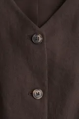 Chaleco largo marrón con escote en V, cierre frontal con botones y bolsillos insertados. Forrado.