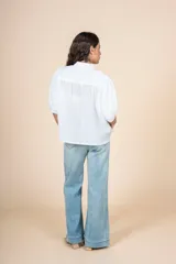 Blusa blanca con detalles bordados en toda la superficie, cuello levemente subido y botones al frente.