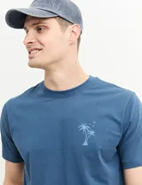 Remera verde con estampado en la espalda de una playa con palmeras y la frase "Ride the waves".