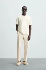 Camiseta color crudo de corte relaxed fit, con cuello redondo y mangas cortas. Presenta un pequeño bordado de flores en el pecho y un estampado fotográfico en la espalda.