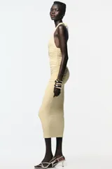 Vestido midi color crema de poliamida con cuello halter con lazada, escote pico pronunciado, detalle de pieza metálica y tejido con frunces.