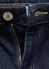 Pantalón de jean azul oscuro, tiro alto, corte mom fit, cinco bolsillos y cierre con cremallera y botón.
