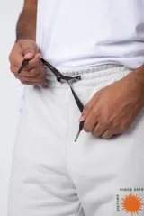 Pantalón de jogging gris claro con puños elásticos, cintura con cordón ajustable y estampado con motivos geométricos en la pierna izquierda.