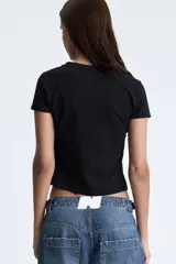 Top de manga corta color negro, ajustado al cuerpo, con cuello redondo y estampado frontal de un corazón rojo con efecto de rejilla y texto en cursiva.