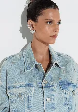 Campera cropped de denim celeste con tachas plateadas formando el logo de la marca.