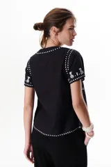 Blusa negra con bordados blancos de animales y motivos geométricos. Tiene cuello redondo con lazo y mangas cortas.