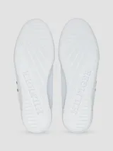 Zapatillas urbanas de corte bajo, color blanco, con cordones y suela de goma. Presentan un gran logo 'H' en color azul marino en el lateral y detalles en azul marino en el talón y la lengüeta.