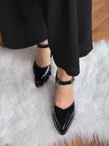 Sandalias negras de charol con punta fina, tira al tobillo con hebilla y tacón bajo.