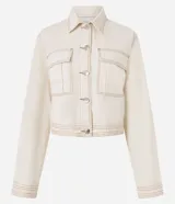 Campera color crudo de manga larga, confeccionada en sarga de algodón, con cuello inglés, abotonada al frente, bolsillos con solapa en el pecho y costuras contrastantes en color marrón.