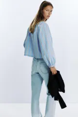 Camisa celeste con rayas verticales marrones y blancas, cuello redondo con escote en pico y mangas largas abullonadas. Cierre frontal con lazos con pespuntes marcados.
