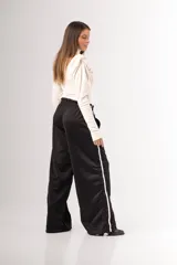 Pantalón negro de tela deportiva con cintura elástica ancha y cordón ajustable. Presenta corte amplio, bolsillos laterales y una franja blanca vertical a lo largo de cada pierna.