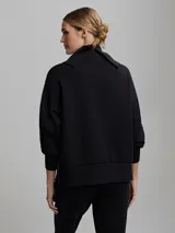Buzo negro de corte oversize con cuello alto, mangas abullonadas, cierre lateral y hombros caídos.