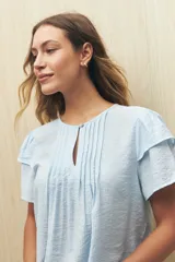 Blusa blanca de tela liviana con mangas cortas con volados y botón de nácar.