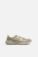 Zapatilla deportiva tipo running de color negro, perteneciente a la colección especial Origins. Presenta una parte superior confeccionada en una combinación de cuero con acabado de gamuza y tejido transpirable. Cuenta con una suela de volumen con diseño irregular y cierre mediante cordones.