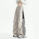 Pantalón deportivo unisex color beige, de corte ancho, con bolsillos laterales tipo cargo, cintura elástica ajustable con cordón, cierre lateral completo y detalle de tres rayas verticales negras en el lateral.