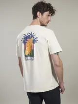 Remera color crema de algodón, con cuello redondo y mangas cortas. Estampado en la espalda con diseño de palmeras, tabla de surf y la palabra 'Mallorca'.