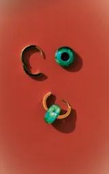 Aros tipo argolla dorados con dije colgante de piedra o vidrio tallado color verde esmeralda con vetas claras.