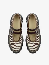 Zapato tipo bailarina con plataforma gruesa y suela flexible. Presenta un diseño con estampado animal print de cebra en tonos crema y marrón, ribete de terciopelo y dos correas de cuero con hebillas plateadas sobre el empeine para un ajuste seguro. Está confeccionado en una combinación de cuero de oveja y vacuno.