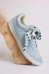 Zapatillas bajas de gamuza celeste con cordones y pañuelos estampados atados a los cordones.