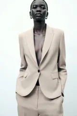 Blazer color beige de corte entallado, con cuello solapa y mangas largas. Tiene bolsillos con solapa en la parte delantera y cierre cruzado con botones.