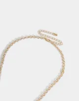Collar corto dorado con cadena de eslabones y dijes colgantes: corazón labrado, mariposa, perlas, cuentas de cerámica con flores y moño.