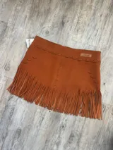 Pollera corta de gamuza color terracota/óxido, con detalle de costuras y apliques de cordones cruzados en la parte superior. El ruedo presenta flecos largos que aportan movimiento.