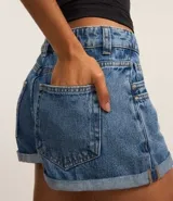 Short de jean de tiro alto, corte slim, con trabillas en la cintura, cierre tradicional, bolsillos y colgante de flor.