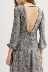 Minivestido plateado con lentejuelas, mangas largas acampanadas y cinturón negro con hebilla dorada en forma de corazón.