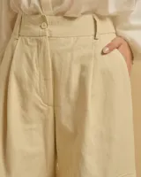 Pantalón acampanado color beige con pinzas, bolsillos italianos y bolsillos de parche con solapas en los laterales. Cierre con botones y cintura con trabillas.