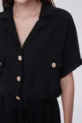 Mono corto negro con cuello camisero, cierre frontal con botones, mangas cortas, dos bolsillos con solapa en el pecho y cintura ajustable con cordón.