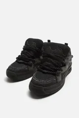 Zapatilla deportiva estilo skate, color negro y gris. Parte superior fabricada en combinación de piezas y materiales. Lengüeta acolchada. Detalle de cordones de cuerda. Tirador trasero para facilitar el calce. Piso con volumen y diseño irregular.