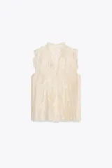 Blusa color crema semitransparente sin mangas, con cuello alto y volantes en el frente y los hombros.